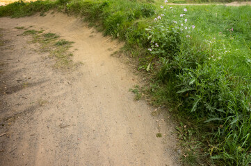 Winding sandy path through green meadow invites exploration on summer day