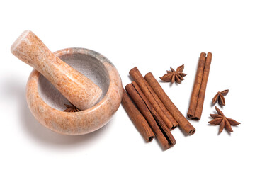 Mortar and pestle with cinnamon and star anise on white background.