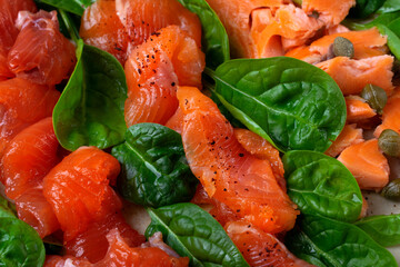 Cold smoked trout fillet sliced ​​and sprinkled with spices on a ceramic plate, served with spinach