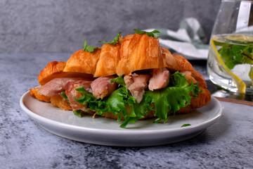 Croissant sandwich with pieces of hot smoked fish catfish clarias on grey table