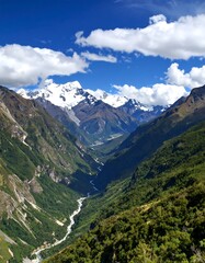 Obraz premium Panoramic view of a lush green valley, a river snaking through it, snow-capped mountains in the background under a vibrant blue sky
