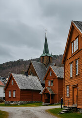 Obraz premium Wooden buildings in a Scandinavian village with a church spire. Tourists standing outside the buildings, observing the historic architecture. Residents of a quaint Norwegian town -