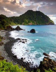 Serene coastal scene at dawn, dark pebble beach, turquoise water, lush green hill