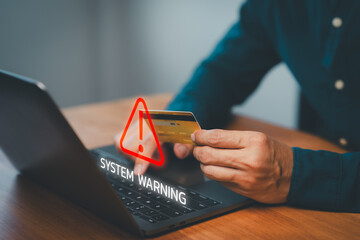 Male hand holding a credit card while using a laptop with warning symbol, representing online...