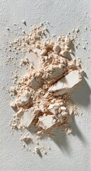 A pale beige powder, coarsely textured, lies in a haphazard pile on a light grey surface, casting a subtle shadow
