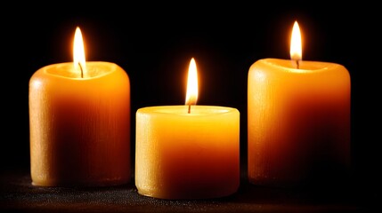 Three illuminated candles against a dark background.