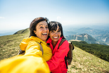 Two senior women taking selfie on top of the mountain - Happy aged female friends having fun on trekking excursion - Sport and tecnology life style concept