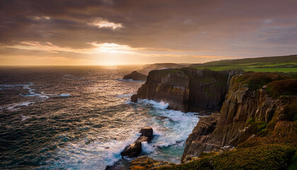 Dramatic sunset view over ocean cliffs with waves crashing against rocks