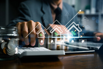 Real estate investment and mortgage calculation concept with businessman using calculator, coins stacked on desk, laptop, and small house model, representing property finance, budget planning, and hom