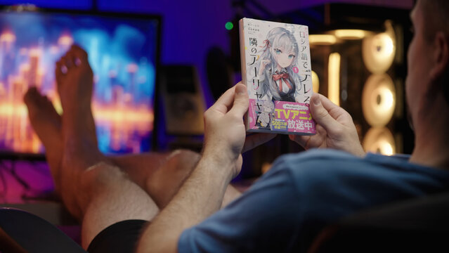 Reading Japanese manga Alya Sometimes Hides Her Feelings with pc in background, over shoulder view