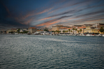 Obraz premium Colorful buildings lining zadar waterfront at sunset, with boats moored in the harbor and dramatic sky reflecting in the adriatic sea