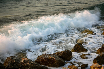 White foamy ocean waves crashing against rocks on the coastline at sunset
