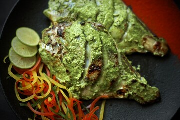Pomfret fish served with green sauce on a black plate in a restaurant background