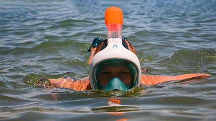 Tourist snorkeling in the sea wearing a full face mask and fins