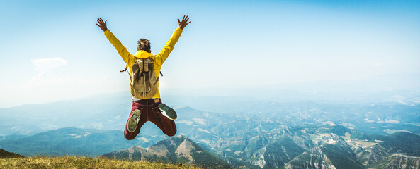 Happy man with backpack jumping on top of the mountain - Delightful hiker with arms up standing over the cliff - Sport and travel life style concept