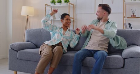 Happy family couple falls and relaxing on sofa, giving high five at home, enjoying fun leisure, sharing joyful moments together, engaging in lively interaction with excitement and connection.