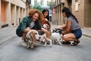 Group of young dog walkers petting basset hounds in a city street