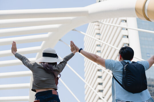 A young couple on vacation stands with their arms raised in an urban setting, celebrating their successful trip. The image captures the joy, freedom, and excitement of modern travel and exploration. - Powered by Adobe