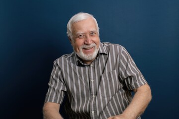 Smiling elderly man in a striped shirt against a dark blue background