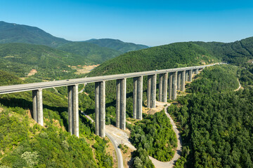 Aerial view of a highway viaduct bridge spanning a lush green mountain valley. Modern transportation infrastructure, engineering. Road trip travel