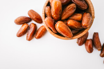 Whole dates in a round wooden bowl with some scattered around, placed on a clean white background. Minimalist, healthy food concept with natural dried fruit