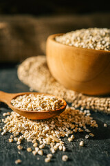Wooden spoon filled with steel-cut oats, scattered grains on dark table, wooden bowl and burlap background. Rustic natural food scene with warm tones