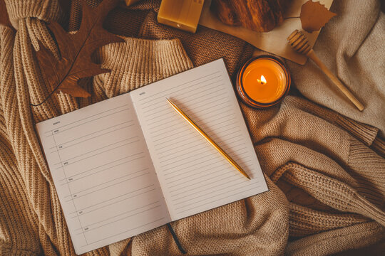 Cozy autumn-themed flat lay with an open weekly planner showing blank days on the left page and a lined “Notes” section on the right. A golden pen rests diagonally across the notes page