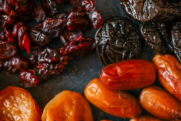 Four types of dried fruits-cranberries, dates, prunes, and apricots-arranged in rows on a dark textured background. A colorful and healthy assortment of natural snacks