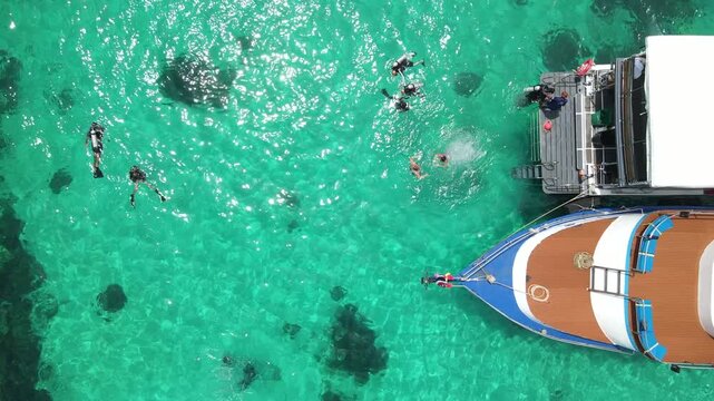 Aerial footage of scuba divers swimming on the surface and climbing up on boat platform at Koh Racha Island, A popular destination for summer activity and scuba diving trip in Phuket, Thailand.