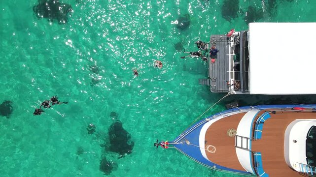 Aerial footage of scuba divers swimming on the surface and climbing up on boat platform at Koh Racha Island, A popular destination for summer activity and scuba diving trip in Phuket, Thailand.