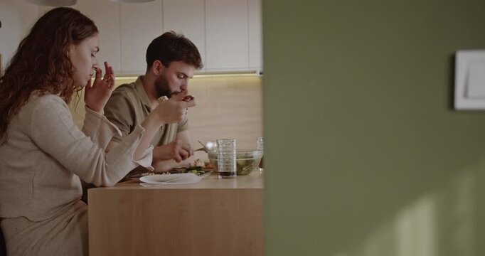 A young couple enjoys a healthy meal together in their modern kitchen, sharing conversation and creating a warm, intimate atmosphere.