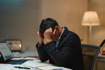 Stressed businessman holding his head in hands at office desk at night