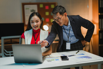 Asian businesspeople working late using laptop in office at night, collaborating on a project