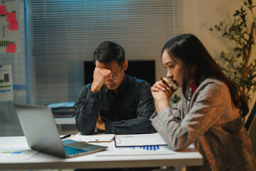 Stressed business team working late reviewing financial reports in office meeting