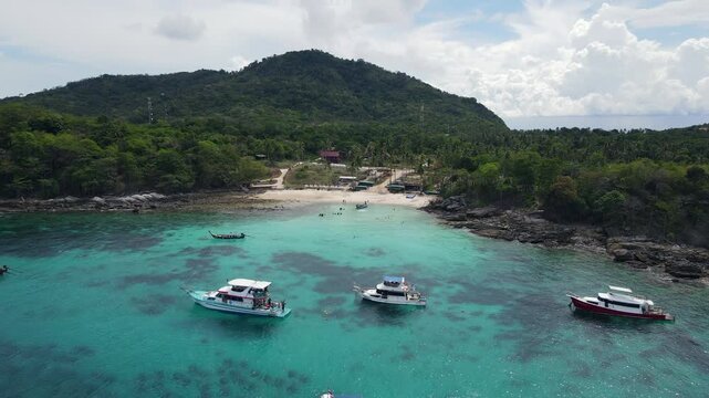 Aerial drone footage of Koh Racha Yai Island with many tour boats, yacht, catamaran and longtail boat anchoring around the bay. A popular destination for summer vacation activity in Phuket, Thailand.