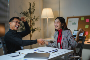 Asian businesspeople shaking hands celebrating successful deal in office at night