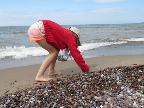 Young Girl in Red Sweater Picking Searching for Rocks and Beach Glass along Shore of Lake Superior in Michigan's Upper Peninsula U.P.