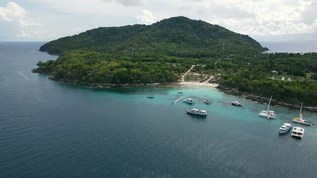 Aerial drone footage of Koh Racha Yai Island with many tour boats, yacht, catamaran and longtail boat anchoring around the bay. A popular destination for summer vacation activity in Phuket, Thailand.