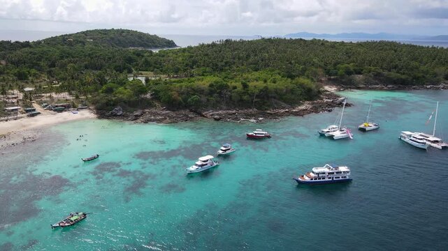 Aerial drone footage of Koh Racha Yai Island with many tour boats, yacht, catamaran and longtail boat anchoring around the bay. A popular destination for summer vacation activity in Phuket, Thailand.