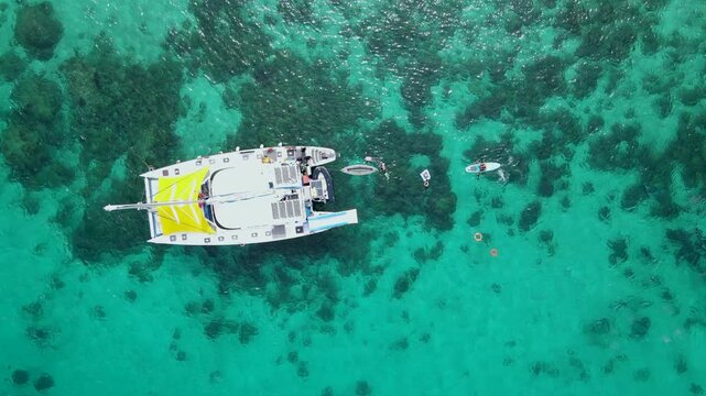 Aerial top view footage of sailing catamaran anchor over turquoise water with tourists swimming and paddle boarding at Racha Yai Island, A popular destination for summer vacation in Phuket, Thailand.