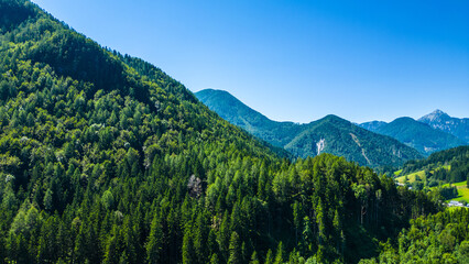 Aerial panoramic view of Zgornje Jezersko valley with lush green meadows, winding roads, and surrounding Kamnik-Savinja Alps under a clear summer sky in Slovenia. Scenic mountain landscape