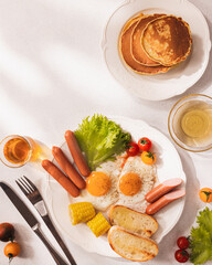 hearty american breakfast plate with fried eggs, sausages, toasted bread, corn, cherry tomatoes, lettuce and pancakes, bright morning sunlight, cozy home brunch, inviting comfort food concept