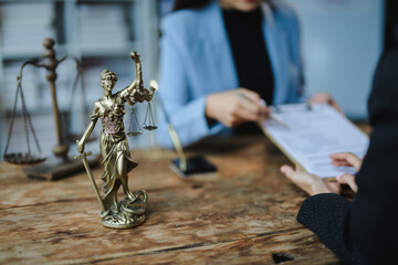 Lawyers discussing contract with justice goddess statue on wooden table