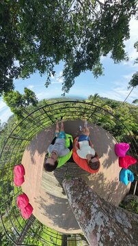 Vertical video. Man and Woman Sitting on Colorful Bean Bags with Tree Branch Arching Overhead in Tiny Planet View, Tiny Planet Effect, Shared Escape Concept