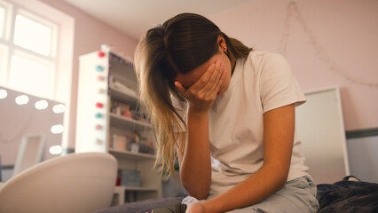 Depressed Teenage Girl Sitting On Bed At Home With Head In Hands