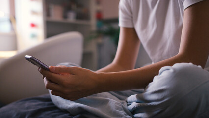 Close Up Of Teenage Girl Sitting On Bed At Home Looking At Mobile Phone