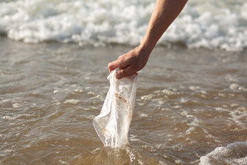Close-up of a hand picking up a plastic bag from the ocean, symbolizing environmental cleanup.