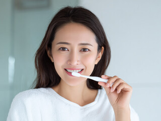笑顔で白い歯を歯ブラシで歯磨きをする日本人女性美人モデルの写真。オーラルケア、デンタルケア、歯科、広告用。