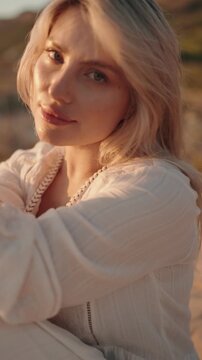 Confident young woman smiles slightly at the camera as the golden light of sunset glows on her face.