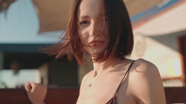 A stylish young woman with a bob haircut enjoys the summer breeze on a sunny day, her hair blowing gently in the wind.